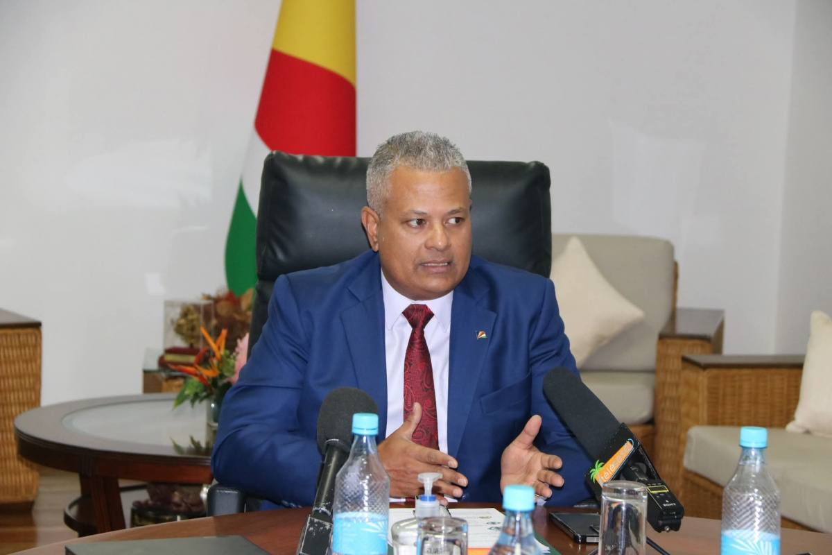 Vice-President Sebastien Pillay speaks at a table with microphones, with the Seychelles flag behind him.